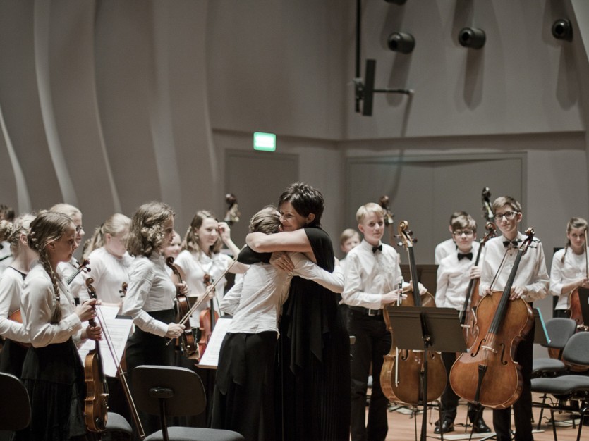 Dyrygentka przytula koncertmistrzynię młodzieżowej orkiestry symfonicznej na estradzie sali kameralnej NOSPR po zakończonym koncercie.
